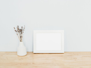 Photo frame mock up. White frame with lovely flowers on the table. Frame mockup with empty space for art, design.