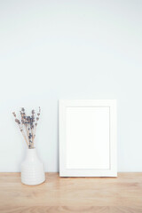 Photo frame mock up. White frame with lovely flowers on the table. Frame mockup with empty space for art, design.