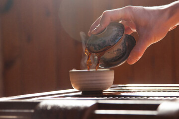 hand pours black chinese tea into a glass teapot