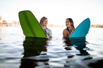 Smiling women in swimsuits sits on their surfboards on the river water