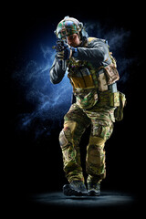 Army soldier in Protective Combat Uniform holding Special Operations Forces Combat Assault Rifle on dark background