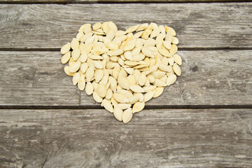 The heart is laid out of pumpkin seeds on a wooden background close-up. Unusual, useful, raw food, love