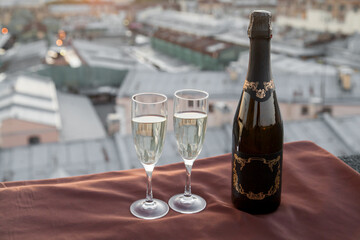 A bottle and two glasses of champagne and against the backdrop of city rooftops at sunset