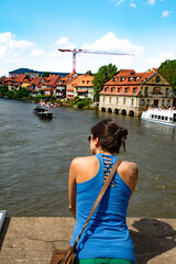 Bamberg, Germany;  young woman siting on a bridge ofer the river Regnitz as it flows through Bamberg, Germany. It is a UNESCO World Heritage Site
