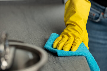 Woman's hands in yellow gloves cleaning counter top in kitchen