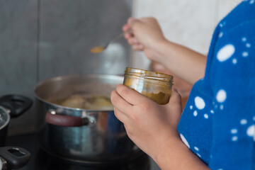 person in blue clothes holding yellow seasoning in their hands while boiling a pot