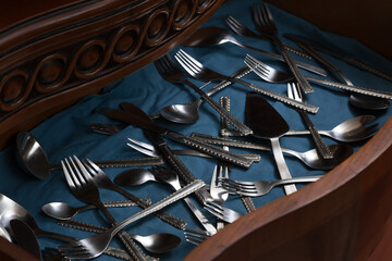 Carved wooden crate with scattered silver cutlery with turquoise background, studio