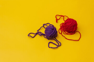 on a yellow background is a red and blue ball of woolen thread, the thread is slightly unraveled and lies on the ground