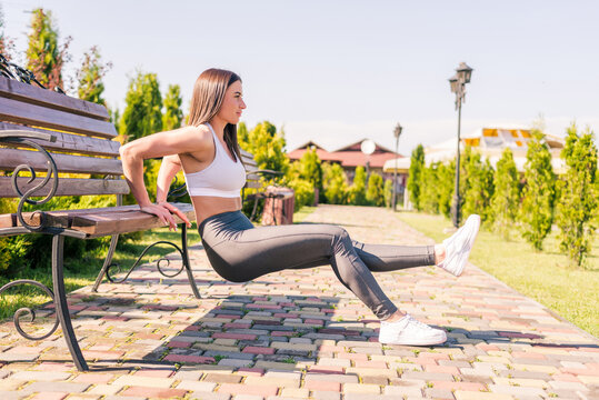 Fitness, sport, training, park and lifestyle concept. Young smiling woman doing push-ups on bench outdoors