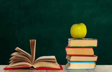 Open book textbook, pile of books and green apple on a wooden desk on the background of a green school chalkboard. Back to school distance home education.Quarantine concept of stay home.