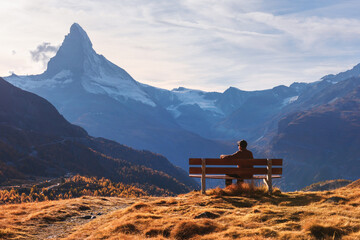 Picturesque view of Matterhorn peak and tourist sitting on wooden bench in Swiss Alps. Zermatt...
