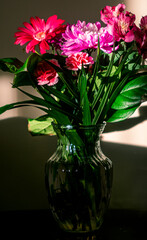 Bouquet of flowers in a glass vase in a corner in a strip of light and shadow