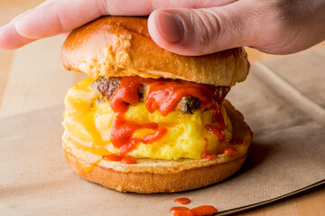Breakfast sandwich. Bacon, fried egg, lettuce, tomato and onion on a bun being smashed by a waitresses hand. Action shot.
