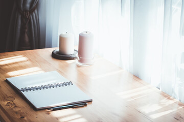 Beautiful study and work concept. Open notebook with white pages, candles, on the wooden table near the window. Notebook, planning, morning, day, sunny, table. Morning, sunny day.