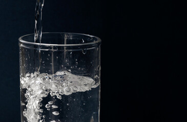 Obraz na płótnie Canvas Pouring water into a glass on a dark blue background