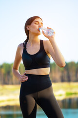 Beautiful young girl athlete drinks water from bottle in nature