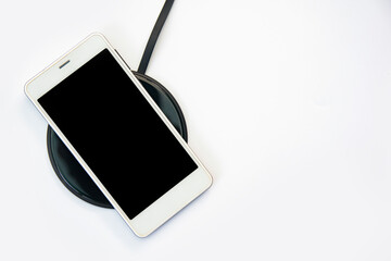 Smartphone charging on a wireless charger on white background. black screen or blank screen with...