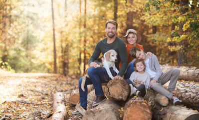 Beautiful young family with small children and dog sitting in autumn forest.