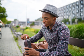 Cheerful young black man commuter sitting on bench outdoors in city.