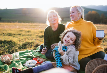Small girl with mother and grandmother having picnic in nature at sunset.