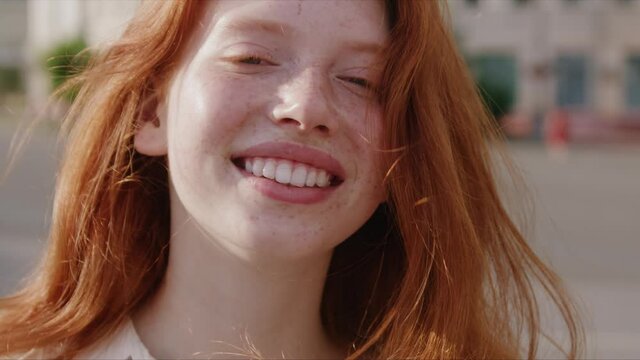 Close up face young sunshine woman with red hair look at camera smile stand in the city streets freckles summer beautiful lady portrait happy outdoor slow motion