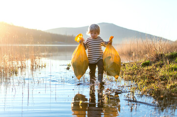 Small child collecting rubbish outdoors in nature, plogging concept.