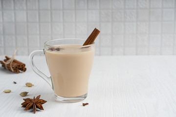 Hot indian masala chai or mixed spice tea made with milk and various aromatic herb such as anise and cinnamon in glass cup on white wooden background at kitchen. Image with copy space