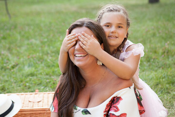Naklejka premium Cute happy young girl covering her mom eyes with her hands, surprising her at the park