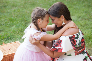 Fototapeta premium Mother and daughter hugging and cuddling head to head outdoors at the picnic