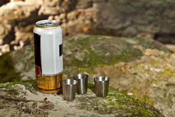 A can of beer with iron cups on a stone. Drinking alcohol in nature.