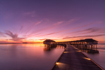 Obraz premium Sunset on Maldives island, luxury water villas resort and wooden pier. Beautiful sunset sky and clouds and tropical beach background for summer vacation holiday and travel concept banner 