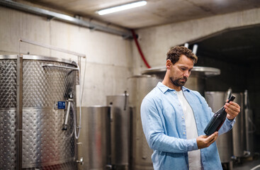 Man worker holding bottle indoors, wine making concept.