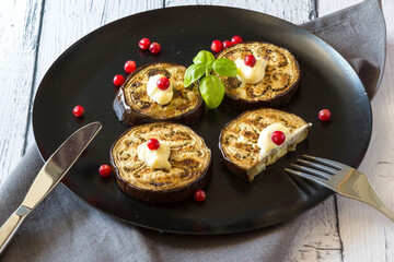 Fried eggplant stuffed with cranberries, garnished with Basil leaves on a dark plate over wooden background. Top view.