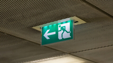 Illuminated emergency exit sign. Green sign with white arrow and figure running to the left. Symbol...