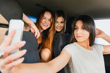 Three happy smiling female travelers posing together for mobile photo about wonderful road trip, selfie with friends, happy memories.