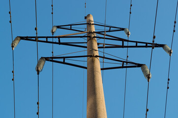 Concrete gray round electric pole with transverse brown metal diamond-shaped frames construction...