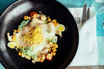 Croutons, tomatoes, eggs, cheese and herbs salad in a dark plate next to the cutlery