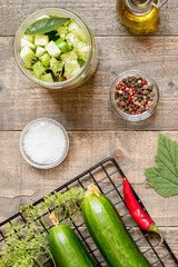 Top view jar with canned cucumbers and seasonings on wooden kitchen table. Food preservation and conservation concept.