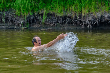 Fototapeta na wymiar Senior man swimming in the taiga Siberian river Vagai, Russia.