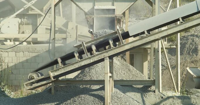Stone crusher plant machine in the work process. Line production for gravel pebbles. Crushing rocks falling from the hopper feeder on the conveyor belt and pile, close-up shot.