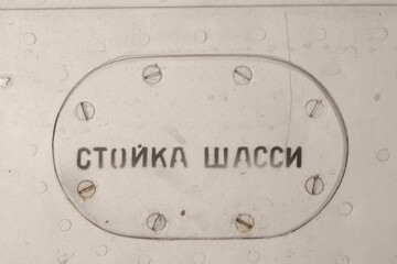 Old silver metal surface of the aircraft fuselage with rivets. The inscription in Russian "landing gear"