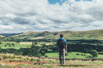 Fototapeta premium Man is observing beautiful field view on Edale village and Mam Tor at Peak District National Park, England, UK while hiking. Staycation concept of traveling local