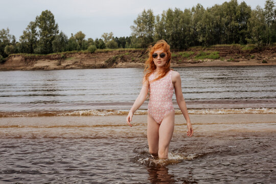 Red-haired girl in a swimsuit stands in the water