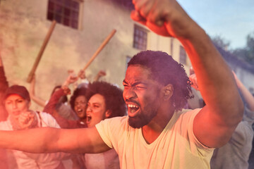 Angry African American activist protesting with crowd of people on city streets.