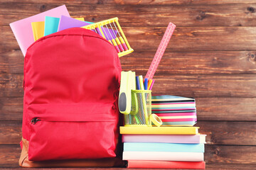 Backpack with school supplies on brown wooden background