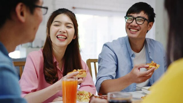 Happy young friends group having lunch at home. Asia family party eating pizza food and laughing enjoying meal while sitting at dining table together at house. Celebration holiday and togetherness.