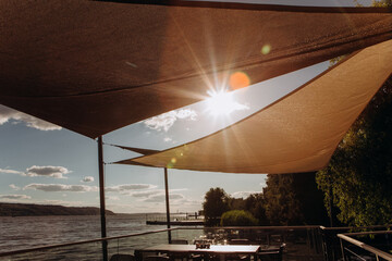 restaurant terrace seashore ray sun through awning - obrazy, fototapety, plakaty