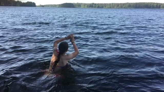 Preteen girl jumping high from water and falling plop into the water, slow motion view. Forest lake