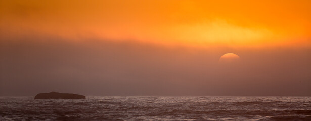 Fototapeta premium The setting sun slips behind a band of clouds at Ruby Beach in Olympic National Park.