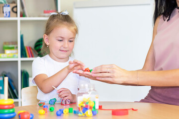 Obraz na płótnie Canvas developmental and speech therapy classes with a child-girl. Speech therapy exercises and games with beads. The girl has beads in her hands